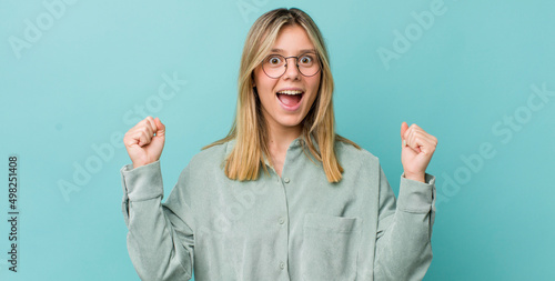 young pretty blonde woman feeling happy, surprised and proud, shouting and celebrating success with a big smile