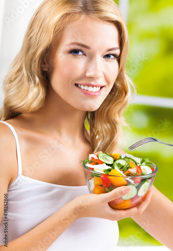 Portrait of happy smiling young woman with vegetable salad near window, indoors. Healthy eating, vegetarian, keto ketogenic diet concept.