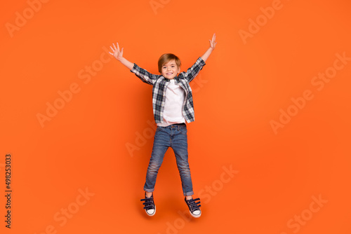 Full length photo of young cheerful boy have fun jump up wear modern outfit isolated over orange color background