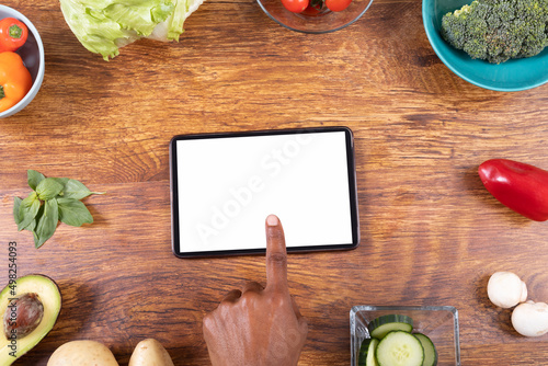 Directly above shot of cropped hand using tablet pc amidst various food on wooden table, copy space