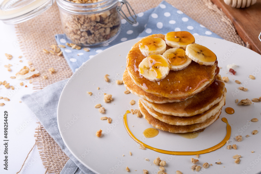 High angle view of pancakes served with banana slices, oats and honey in plate on napkin High angle view of pancakes served with banana slices, oats and honey in plate on napkin