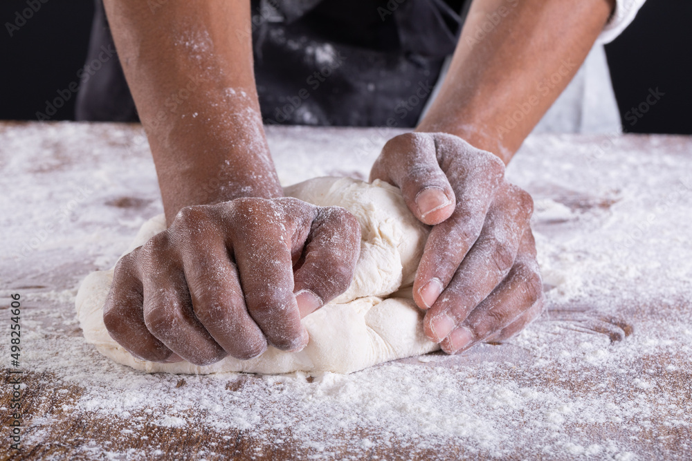 Cropped hands of african american male baker kneading dough on table