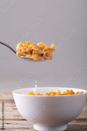 Close-up of cornflakes in spoon over breakfast bowl on table against gray background with copy space