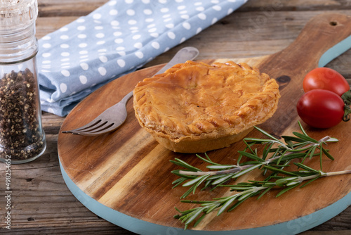 Stuffed pie with rosemary and tomatoes on serving board by black pepper in container at table