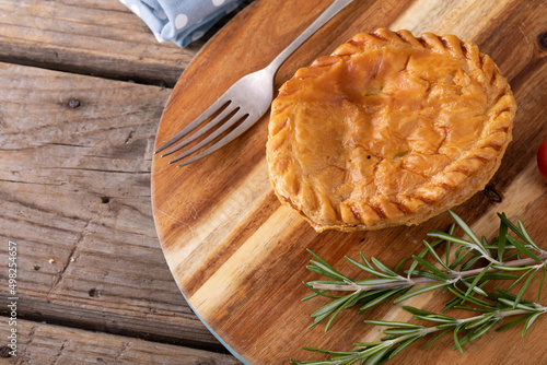 High angle view of stuffed pie with rosemary and fork on wooden serving board at table