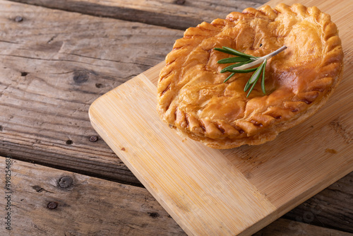 Close-up of baked stuffed pie with rosemary on wooden serving board at table