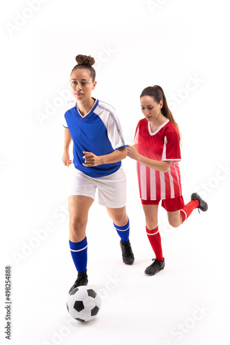 Full length of biracial and caucasian young female players playing soccer against white background