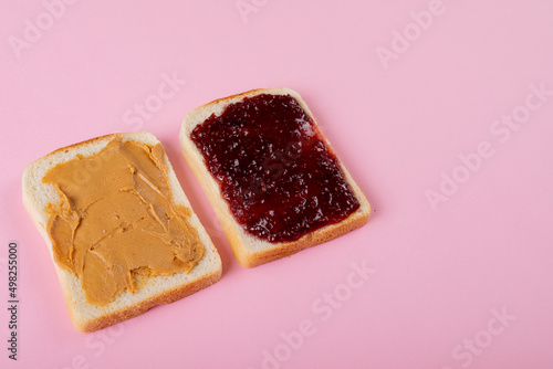 High angle view of peanut butter and preserves on bread slices over pink background