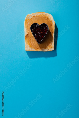 Close-up of jam in heart shape pastry cutter over bread with peanut butter on blue background