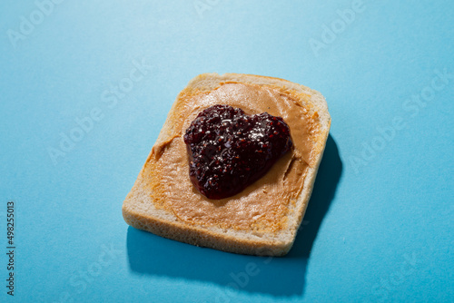 Close-up of preserves and peanut butter on bread slice over blue background with copy space