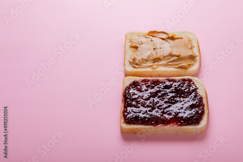 Peanut butter and preserves on bread slices over pink background with copy space