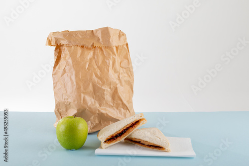 Green apple with peanut butter and jelly sandwich by paper bag at table against gray background