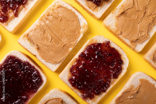 Full frame shot of bread slices with peanut butter and preserves arranged on yellow background