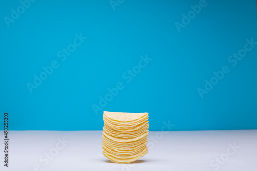 Stack of potato chips on table against blue background with copy space