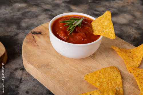 Close-up of nacho chips and red sauce with rosemary herb served on serving board at table