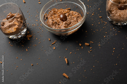 Close-up of chocolate mousse with coated nuts and shredded chocolate served in bowl and glasses