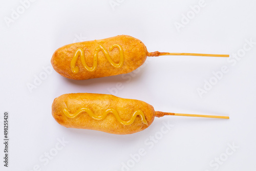 Overhead view of corn dogs over skewers with mustard sauce on white background