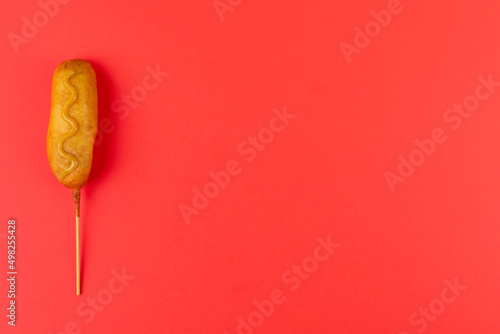 Directly above shot of corn dog with mustered sauce over skewer on red background with copy space