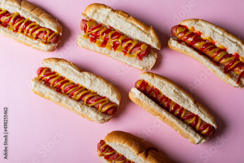 Directly above shot of sauces on hot dogs over pink background