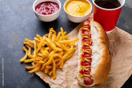 High angle view of hot dog with french fries, sauces and drink on table