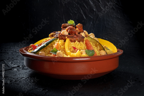 Couscous with meat and vegetables, traditional Moroccan dish, with chickpeas and cilantro, on a black background photo