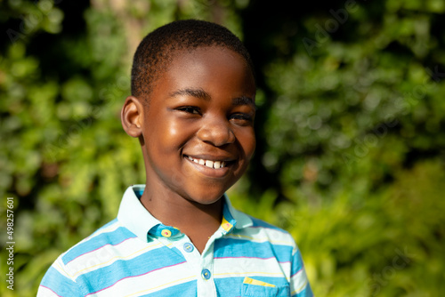 Portrait of cute happy african american boy standing against plants outdoors