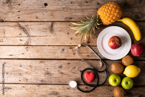 Directly above shot various fruits with stethoscope and heart shape on wooden table with empty space