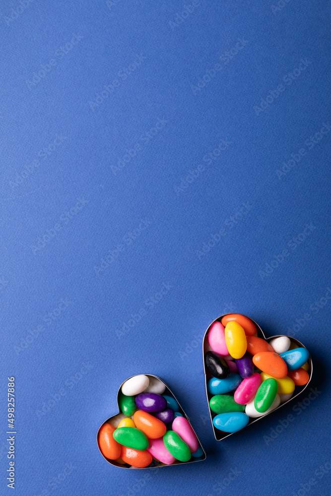 Overhead view of copy space above colorful candies in heart shape containers over blue background Overhead view of copy space above colorful candies in heart shape containers over blue background