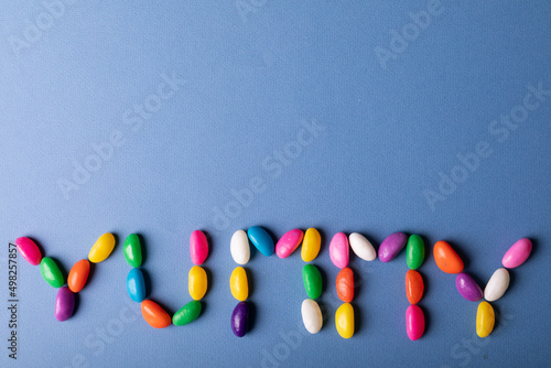 Directly above view of colorful candies arranged as yummy word on blue background with copy space
