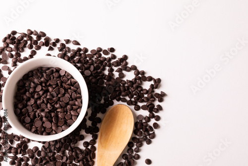 Overhead view of wooden spoon with bowl and chocolate chips by copy space on white background