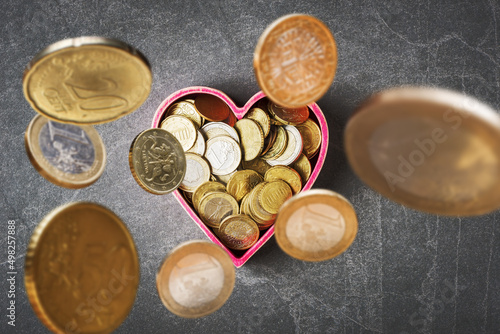 Euro currency coins falling in heart shaped box on grey stone background. Love and money concept