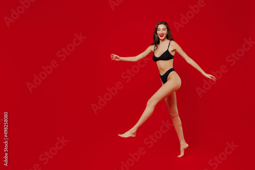 Full body profile happy smiling satisfied fun young sexy woman 20s with perfect fit body wear black underwear jump high isolated on plain red background studio portrait. People female beauty concept