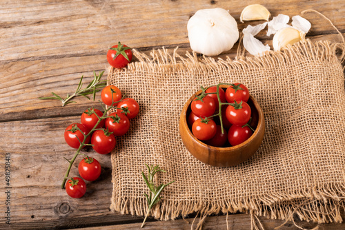High angle view of fresh cherry tomatoes with burlap and garlic bulb on wooden table