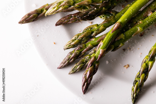High angle close-up view of asparagus and seasoning in plate on white background