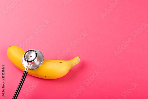 Directly above view of fresh banana with stethoscope by copy space on pink background