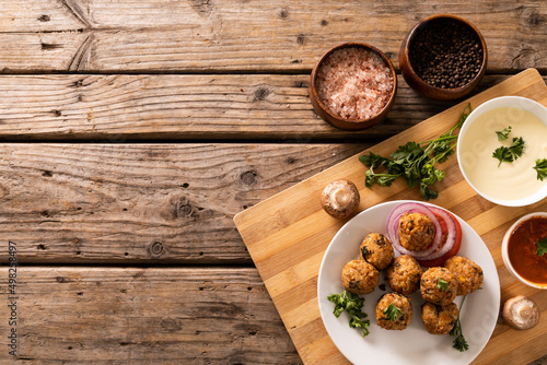 Directly above view of fresh meatballs with seasoning bowls on cutting board over wooden table