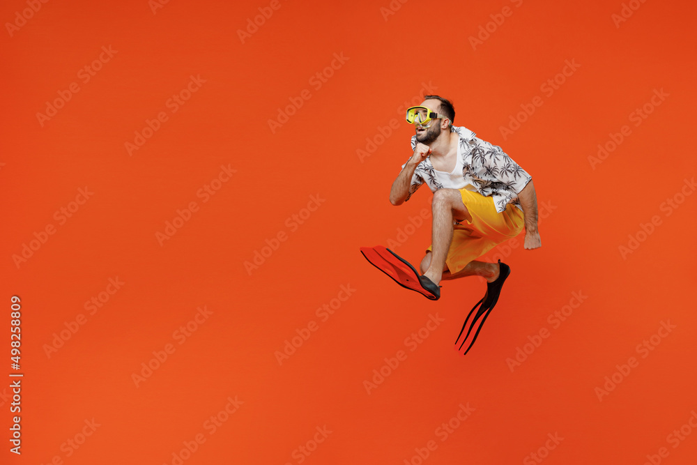 Full body side view young tourist man in beach shirt goggles flippers run fast jump high travel abroad on weekends isolated on plain orange background studio Summer vacation sea rest sun tan concept.