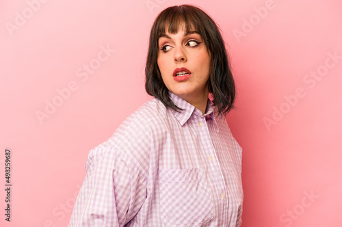 Young caucasian woman isolated on pink background looks aside smiling, cheerful and pleasant. © Asier