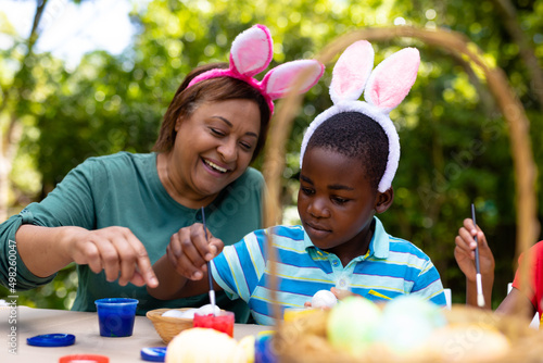 African american boy and grandmother wearing bunny ears while painting eggs on easter day
