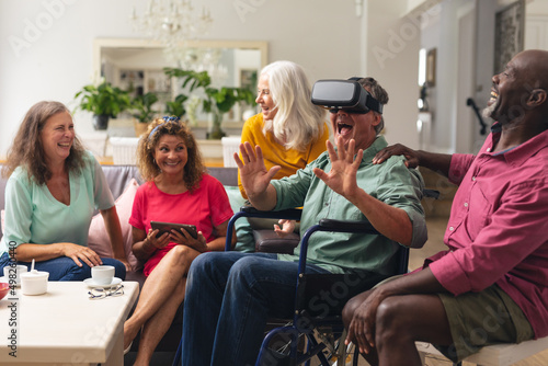 Happy multiracial senior man and woman with handicap male friend using vr headset at home