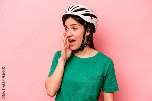 Young caucasian woman wearing helmet isolated on pink background shouting and holding palm near opened mouth.