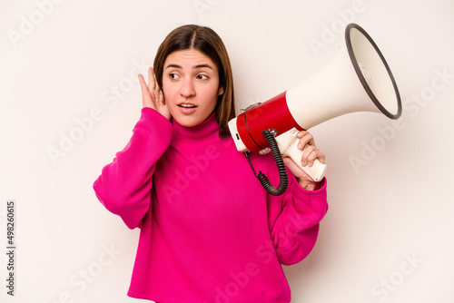 Young caucasian woman holding a megaphone isolated on white background trying to listening a gossip.