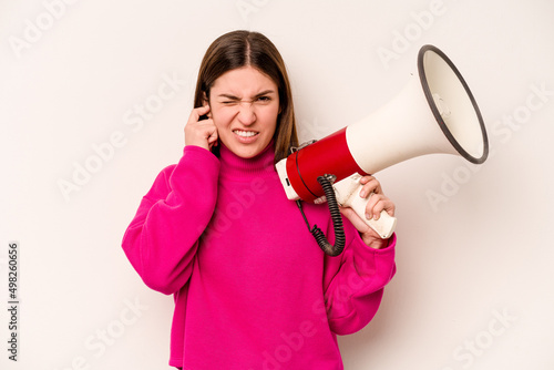 Young caucasian woman holding a megaphone isolated on white background covering ears with hands.