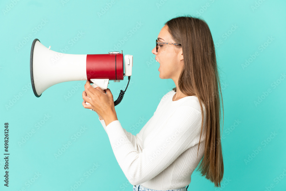 Young woman over isolated blue background shouting through a megaphone to announce something in lateral position Young woman over isolated blue background shouting through a megaphone to announce something in lateral position