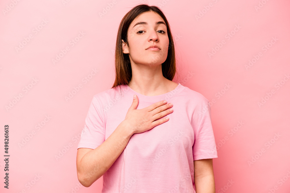 Fototapeta premium Young caucasian woman isolated on pink background taking an oath, putting hand on chest.