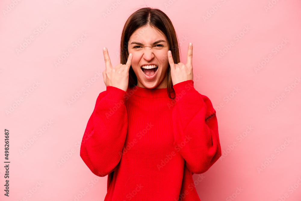 Young caucasian woman isolated on pink background showing a horns gesture as a revolution concept. Young caucasian woman isolated on pink background showing a horns gesture as a revolution concept.