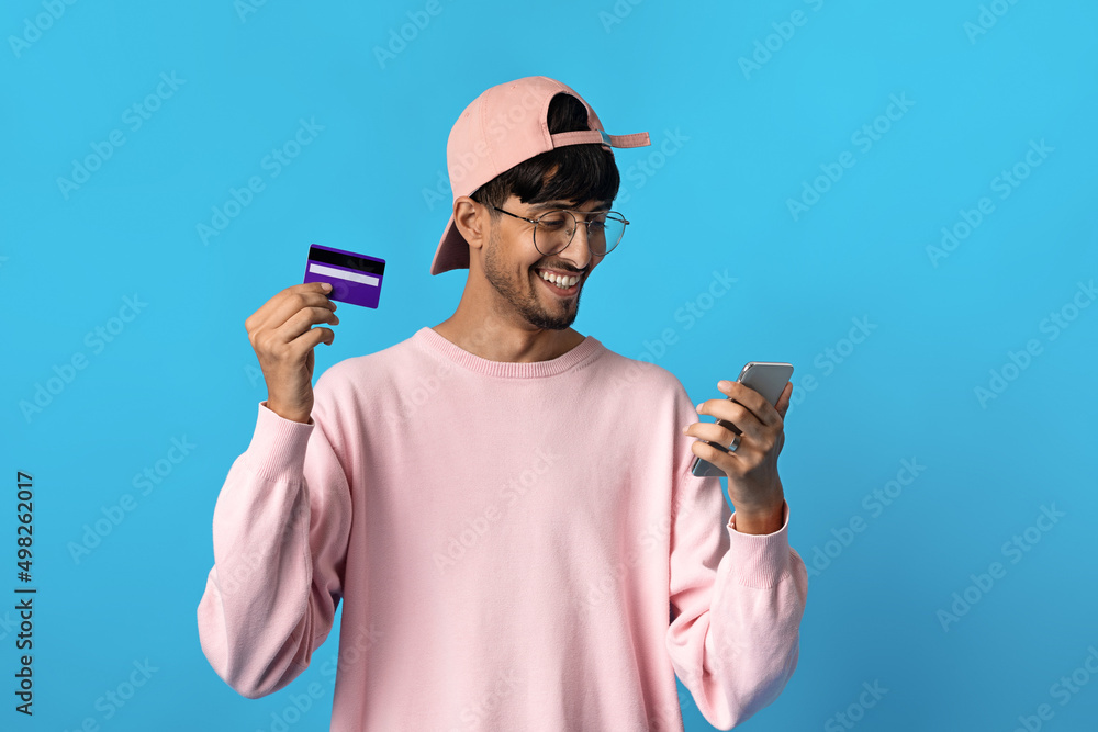 Cheerful indian guy holding cell phone and credit card Cheerful indian guy holding cell phone and credit card