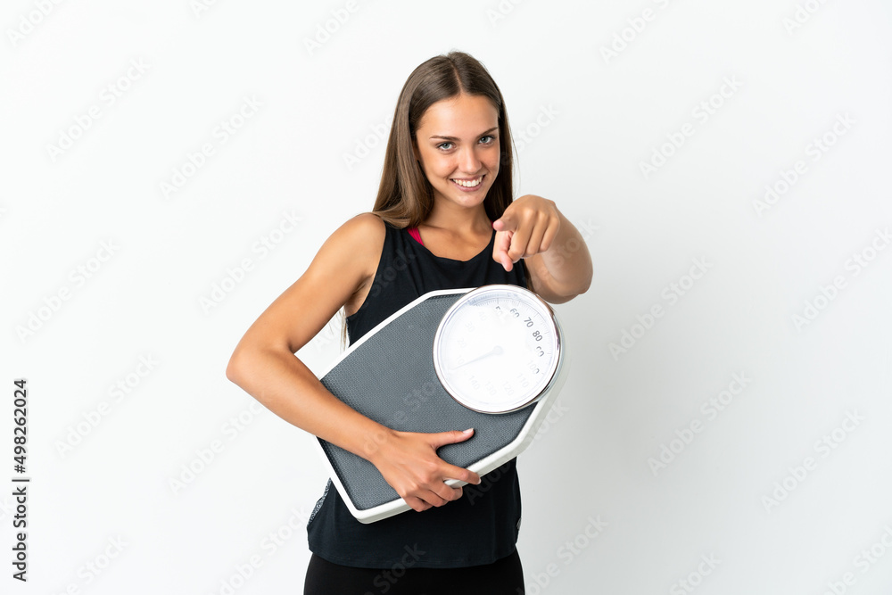 Young woman over isolated white background holding a weighing machine and pointing to the front Young woman over isolated white background holding a weighing machine and pointing to the front