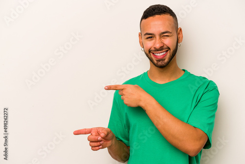 Young hispanic man isolated on white background excited pointing with forefingers away.