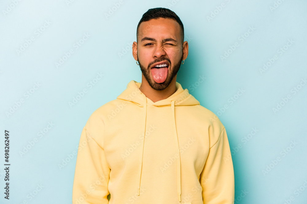 Obraz premium Young hispanic man isolated on blue background funny and friendly sticking out tongue.
